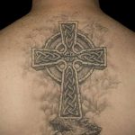 Фото тату кельтского креста на спине мужчины. Черно-серый рисунок с детальной проработкой и облаками.