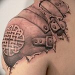 Фото тату кельтского узора на плече, с эффектом "разорванной" кожи, обнажающей металлические детали. Черно-серый рисунок с реалистичной проработкой.