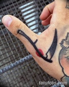 Фото небольшой татуировки косы с красными каплями, имитирующими кровь, на пальце руки. Оригинальный и смелый дизайн.