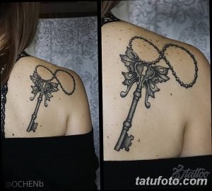 Фото тату старинного ключа с цепочкой на лопатке. Черно-белая татуировка с детальной проработкой узоров.