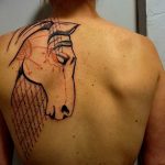 Фото татуировки с изображением головы лошади, выполненной в графичном стиле с использованием черных линий и красных акцентов.