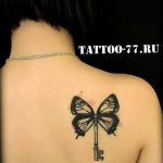 Фото татуировки на спине с изображением бабочки, держащей в лапках ключ. Рисунок выполнен в черном цвете с добавлением небольших красных точек.