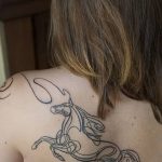 Фото тату кельтского коня на спине, выполненное в стиле трайбл с использованием черных линий и сложных узоров. Элегантный рисунок татуировки.