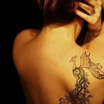 Большая татуировка павлина на спине, выполненная в черном цвете с детализированными перьями и растительными элементами.