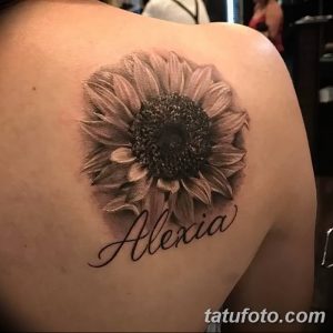 Крупный реалистичный рисунок подсолнуха с надписью 'Alexia' на плече, выполненный в черно-серых тонах.