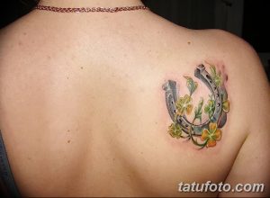 Фото тату с изображением подковы и четырехлистного клевера на женской спине. Рисунок выполнен в ярких цветах.