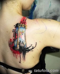Фото тату песочных часов на спине. Изображение выполнено в сочетании черного, красного и голубого цветов с использованием акварельной техники, символизируя течение времени.