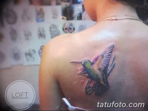 Фото акварельной татуировки колибри на лопатке. Яркие цвета, размытые контуры, создающие эффект живописи.
