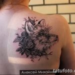 Фото тату: реалистичное изображение головы лисы, окруженной цветами, на плече. Детализированный рисунок татуировки в черно-серых тонах.