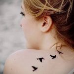 Фото тату трех маленьких птиц на спине девушки. Минималистичный рисунок татуировки в черном цвете. Идея для тату.