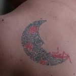 Фото тату в виде полумесяца, заполненного сложным орнаментом, на груди. Рисунок выполнен в черно-красных тонах, с использованием тонких линий и геометрических фигур.