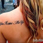 Фото татуировки с надписью "You Raise Me Up" на спине. Изображение выполнено черным цветом в каллиграфическом стиле.