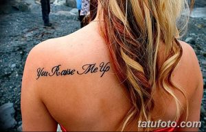 Фото татуировки с надписью "You Raise Me Up" на спине. Изображение выполнено черным цветом в каллиграфическом стиле.