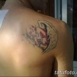 Фото татуировки ангела на лопатке. Изображение выполнено в мягких тонах с использованием розовых и желтых оттенков. Ангел с расправленными крыльями.