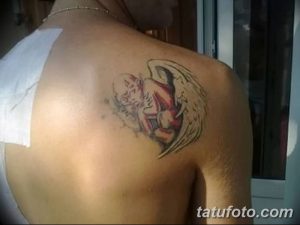 Фото татуировки ангела на лопатке. Изображение выполнено в мягких тонах с использованием розовых и желтых оттенков. Ангел с расправленными крыльями.