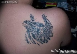 Фото тату дракона на плече. Черно-серый рисунок дракона с расправленными крыльями, детализированная проработка чешуи и морды.