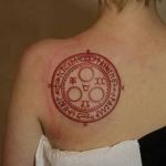 Фото тату на лопатке: красный круг с древними символами и надписями, выполненный в минималистичном стиле. Идеально для любителей оккультизма.