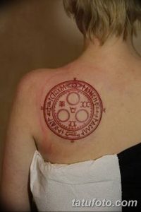 Фото тату на лопатке: красный круг с древними символами и надписями, выполненный в минималистичном стиле. Идеально для любителей оккультизма.