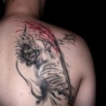 Фото татуировки самурая на плече. Черно-серый рисунок воина с мечом, выполненный в технике с эффектом брызг краски, символизирующий силу и честь.