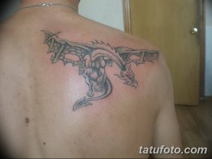 Фото тату дракона на спине. Детализированный рисунок мифического существа в черно-серых тонах, с расправленными крыльями и острыми когтями.