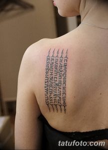 Фото тату: вертикальная колонна древних рун на спине. Минималистичный рисунок татуировки выполнен черными чернилами.