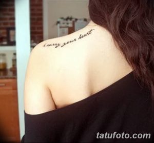 Фото тату: изящная надпись "carry your heart" на плече девушки. Минималистичный рисунок татуировки выполнен черными чернилами.
