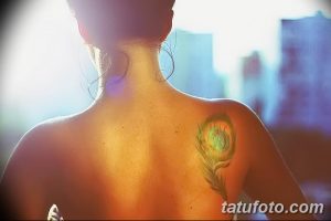 Фото тату: красочное перо павлина на спине девушки. Детализированный рисунок татуировки с яркими цветами и переливами.