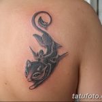 Фото тату: изящная черная кошка с длинным хвостом, выполненная в минималистичном стиле на плече. Четкие линии и лаконичный дизайн.