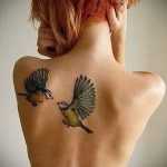 Фото акварельной татуировки с изображением двух птиц на спине девушки. Нежные цвета и плавные переходы создают эффект легкости и воздушности.