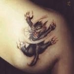 Фото тату: красочный дракон, обвивающий плечо. Детализированный рисунок татуировки с использованием ярких цветов и сложных узоров.