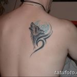 Фото татуировки на спине: изображение воющего волка на фоне луны, выполненное в стиле трайбл с использованием черных и голубых оттенков.