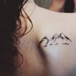 Фото минималистичной татуировки на спине с изображением горных вершин и птиц. Черно-белый рисунок татуировки.