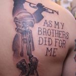 Фото тату на плече с изображением военного, играющего на трубе, и надписью 'As My Brothers Did For Me'. Черно-серый рисунок татуировки.