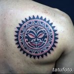 Фото тату в полинезийском стиле на плече. Черно-белый рисунок с красными акцентами, изображающий маску в центре солнечного круга.