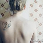 Фото тату: маленькая белая птица с расправленными крыльями на спине девушки. Минималистичный рисунок татуировки, простой эскиз тату.