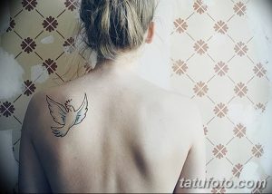 Фото тату: маленькая белая птица с расправленными крыльями на спине девушки. Минималистичный рисунок татуировки, простой эскиз тату.