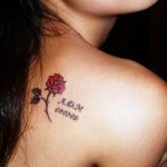 Фото тату розы с надписью 'A.D.M 08.07.09' на ключице. Нежный рисунок татуировки в черном цвете.