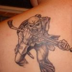 Фото тату на лопатке с изображением Эдди, талисмана группы Iron Maiden. Татуировка выполнена в черно-серых тонах с детальной проработкой.