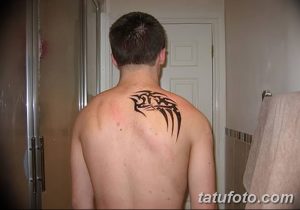 Фото татуировки в стиле трайбл на спине мужчины. Татуировка состоит из черных геометрических узоров и острых линий.