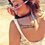Фото тату надписи "Dreams are our escape from reality" на спине. Элегантный шрифт, вдохновляющий смысл. Подходит для мечтательных и творческих людей.