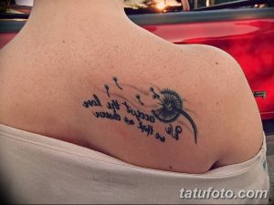 Фото татуировки одуванчика с летящими семенами и надписью на лопатке. Тату выполнено в минималистичном стиле черными чернилами.