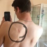 Фото тату: эскиз татуировки в виде незавершенного круга, нарисованный на спине мужчины. Черный контур и минималистичный дизайн.