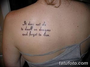 Фото тату: черная надпись на спине 'It does not do to dwell on dreams and forget to live'. Элегантный шрифт и минималистичный дизайн.