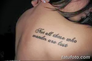 Фото тату: черная надпись на лопатке 'Not all those who wander are lost'. Элегантный шрифт и минималистичный дизайн.