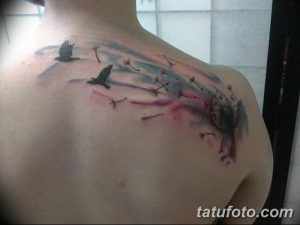 Фото татуировки на спине с изображением одуванчиков и летящих птиц. Рисунок выполнен в акварельной технике с использованием нежных розовых, синих и серых оттенков.