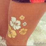 Фото татуировки с изображением цветов в акварельной технике на ноге. Использование различных оттенков желтого, белого и золотого.