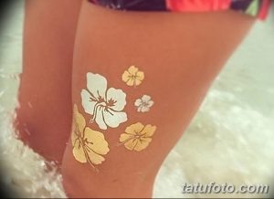 Фото татуировки с изображением цветов в акварельной технике на ноге. Использование различных оттенков желтого, белого и золотого.
