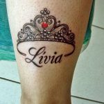 Фото тату: черная корона с красным сердцем и надписью 'Livia' на голени. Детализированный рисунок татуировки, выполненный в стиле blackwork.