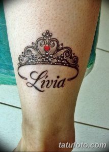 Фото тату: черная корона с красным сердцем и надписью 'Livia' на голени. Детализированный рисунок татуировки, выполненный в стиле blackwork.