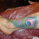 Фото тату: красочное перо павлина на лодыжке. Яркие оттенки синего, зеленого и желтого создают эффектный и запоминающийся образ.